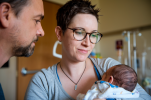 A woman holding a baby in a hospital room with a man standing beside her