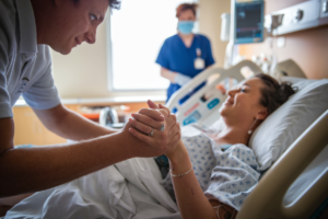 A father holding his wife's hand during childbirth in a hospital setting