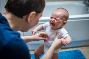 A parent changing a crying baby's diaper in a bathroom