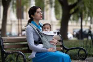 A contemplative mother holding a baby in a park, symbolizing identity crisis in motherhood.