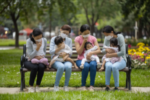 A group of sick mothers sitting on a bench in a park, still taking care of their children.