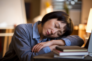A mother resting her head on a table, representing maternal exhaustion in a cozy home setting.