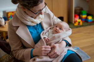 A mother holding her baby in a cozy room with toys and Legos
